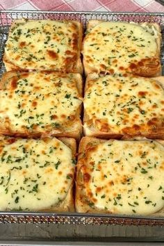 several square pieces of bread with cheese and herbs on them sitting in a metal pan