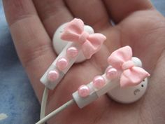 two little pink bows on top of white headphones in the palm of someone's hand