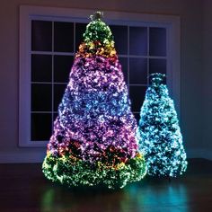 three brightly lit christmas trees in front of a window