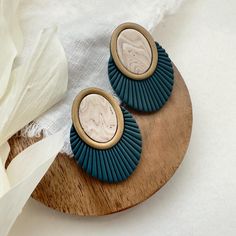 two blue and white earrings on a wooden plate next to some tissue paper, with a flower in the background