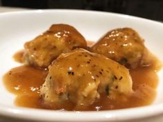 two meatballs covered in gravy on a white plate