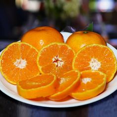 an orange cut in half on a white plate with other sliced oranges around it