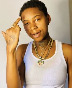 a woman wearing a white tank top holding her hand up to her ear and making the peace sign