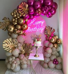 a birthday cake on a table surrounded by balloons and palm leaves, with a neon sign that says happy birthday