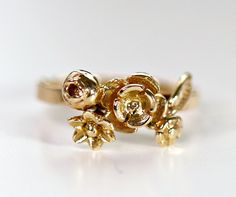 a yellow gold ring with leaves and flowers on the front, set against a white background