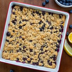 a blueberry crumble cake in a red and white dish next to lemon slices