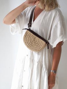 a woman wearing a white dress is holding a straw bag and talking on the phone