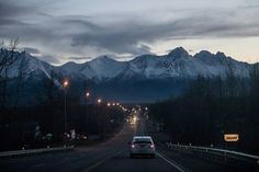 a car is driving down the road in front of some mountains at night with lights on