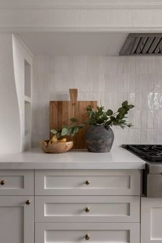 a kitchen with white cabinets and wooden cutting board on the counter top next to a potted plant