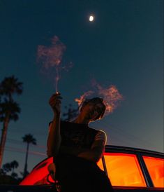 a woman standing next to a red car holding a lit sparkler in her hand