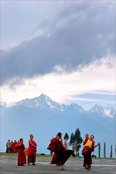 several people in red and yellow robes are walking on the pavement with mountains in the background