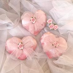 three pink heart shaped boxes with flowers on top of white netted fabric and tulle