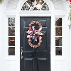 a black front door with a wreath on it and red ribbon hanging from the top