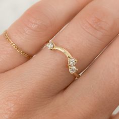 a woman's hand wearing a gold ring with three diamonds on the middle finger