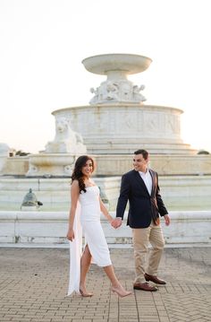 a man and woman holding hands in front of a fountain