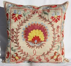 an embroidered pillow with red, yellow and blue flowers on the front is sitting on a white surface