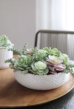 two white vases filled with succulents sitting on top of a wooden table