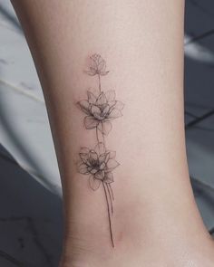 a flower tattoo on the ankle is shown in black and grey ink, with three petals coming out of it