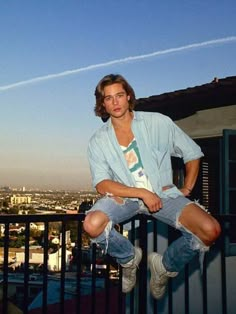 a young man sitting on top of a balcony next to a railing with an airplane in the background