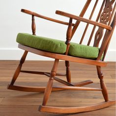 a wooden rocking chair with green cushion on the seat and wood floors in front of a white wall