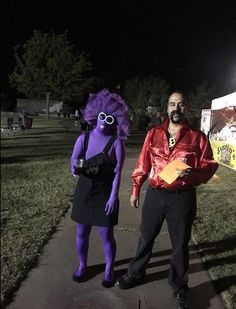 two people dressed in costumes standing on a sidewalk at night, one holding a piece of paper and the other wearing glasses