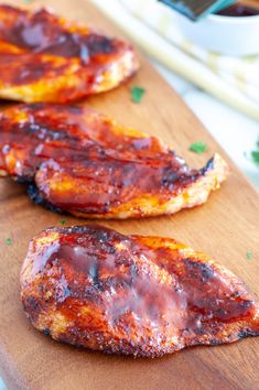 two pieces of meat sitting on top of a wooden cutting board next to some sauce