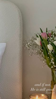 a vase filled with white and pink flowers next to a lit candle