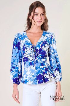 The Coastal blue abstract flowers painted on the Cosette Front Tie Peplum Top makes it timeless. This top features a long balloon sleeve that frames a peplum silhouette. A deep v-neckline is held together by tie details, which then transition to a rouleaux style button front. The top is finished off with a flouncy ruffle waist. Wear it with white bottoms and strappy sandals to match. Rouleaux button front Deep V neckline Peplum waist Tie front details Size + Fit: True To Size. Model is 5'8" and Floral Blouse Outfit, Ann Taylor Outfit, Papaya Clothing, Flowers Painted, White Bottoms, Blue Floral Blouse, Sew Easy, Coastal Blue, Blue Ivory