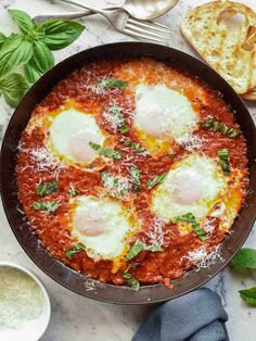 an egg dish in a pan with parmesan cheese and basil on the side