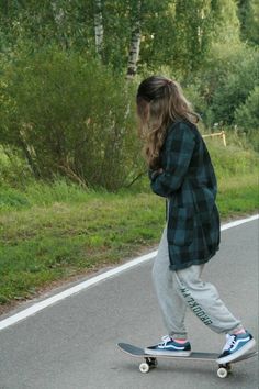 a person riding a skateboard down a road next to some grass and trees in the background