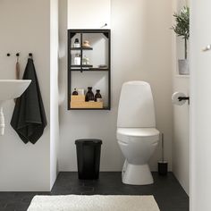 a white toilet sitting next to a black trash can in a bathroom under a window