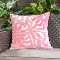 a pink and white pillow sitting on top of a chair next to a potted plant