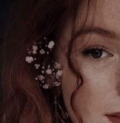 a close up of a woman's face with flowers in her hair and earrings