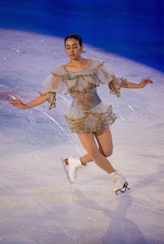 a female figure skating on the ice in a short dress and white tennis shoes with her arms outstretched