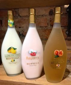 three bottles of wine sitting on top of a wooden shelf next to a brick wall