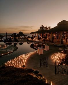 an outdoor dining area with candles lit up in front of the water at night time