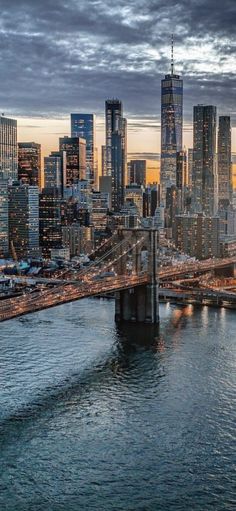 an aerial view of the city skyline at dusk from across the water with a bridge in the foreground