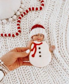 a person holding a small snowman ornament in their hand, on a white knitted blanket