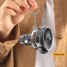 a person holding a keychain that is shaped like an airplane engine and has a jet engine attached to it