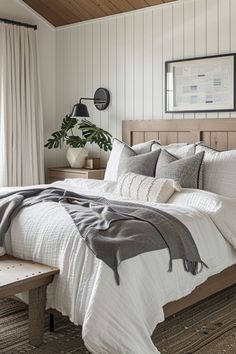 a bed with white sheets and pillows in a bedroom next to a window, potted plant