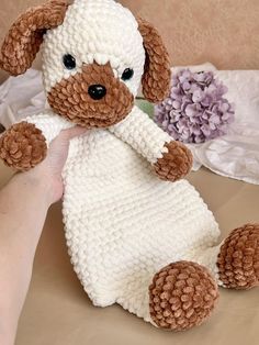 a hand holding a brown and white knitted stuffed dog on top of a bed