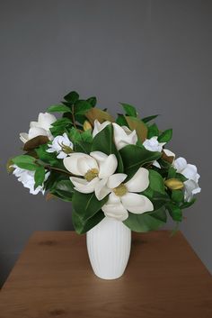 a vase filled with white flowers on top of a wooden table next to a gray wall