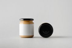 a jar of peanut butter next to a black lid on a white surface with a gray background