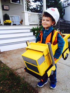 a young boy dressed up as a construction worker holding a cardboard box on his back