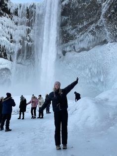 a woman standing in front of a waterfall with her arms up and two children looking on