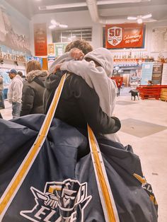 two people sitting on top of a large bag in a store with other people standing around