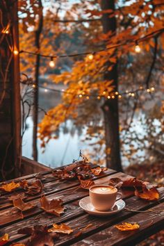 a cup of coffee sitting on top of a wooden table in front of some leaves