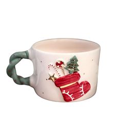 a white cup with a green handle and christmas decorations on the side, sitting in front of a white background