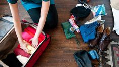 a woman is packing her suitcase on the floor with clothes and other items in it