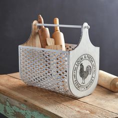 a metal basket with wooden utensils in it on top of a wood table